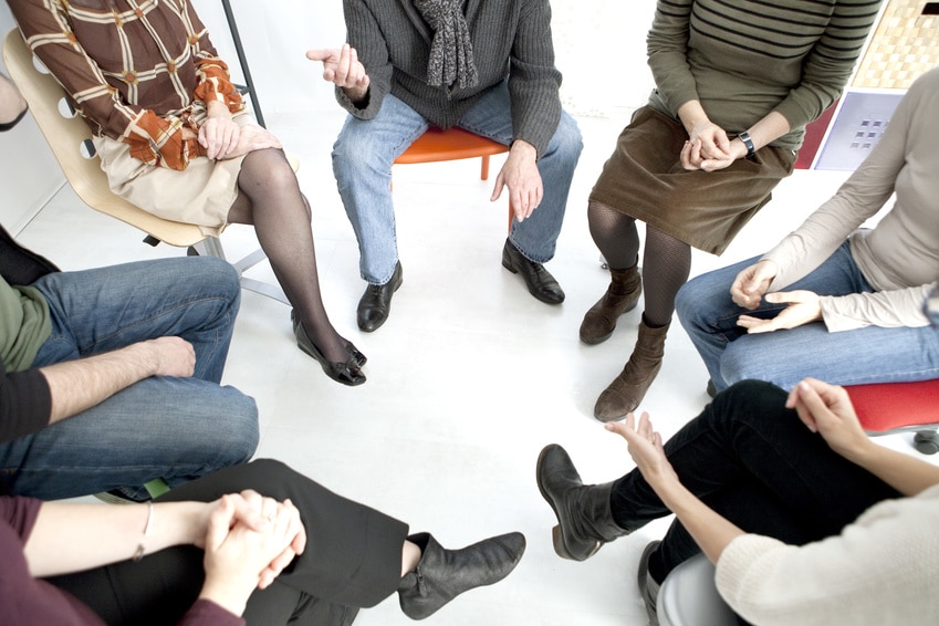 A group of people sitting on chairs, ina circle facing each other talking about a men's health support group